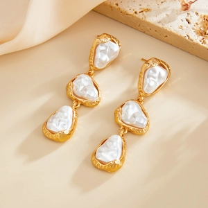 Détail macro de boucles d'oreilles triple perles baroques avec fini doré martelé