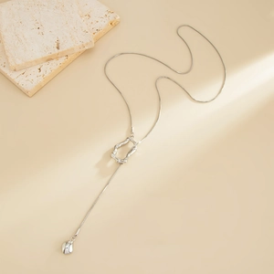 Minimalist Y-shaped silver snake chain necklace with irregular hollow pendant on travertine