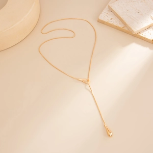 Detail of gold teardrop pendant Y-necklace featuring a sleek snake chain on stone decor