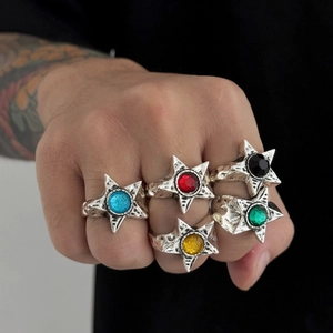 Dettaglio di cinque anelli punk a stella con gemme colorate su un pugno tatuato