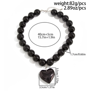 Detalle de collar de cuentas negras grandes con colgante de corazón brillante y cadena