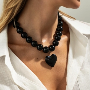Primer plano de collar de cuentas negras con colgante de corazón sobre una camisa blanca