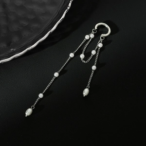 Detail of silver chain ear cuff with long tassels and white pearls on black texture