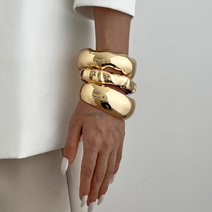 Three irregular chunky gold stacked bracelets in organic mirror finish for a hip-hop style