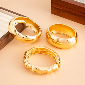Close-up of three stacked gold-plated chunky bangles with polished and textured surfaces