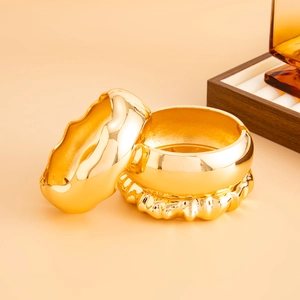 Detailed view of wide gold-plated chunky bangles with polished wavy texture and mirror finish