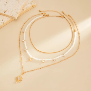 Détail de colliers dorés à trois rangs avec pendentifs étoiles sur fond de pierre beige
