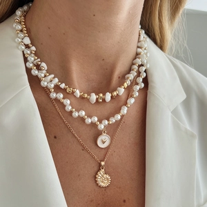 Détail de colliers dorés multicouches avec pierres blanches, perles et pendentifs cœur
