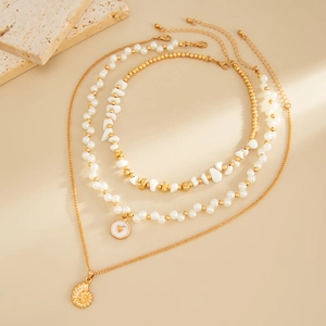 Détail de colliers superposés dorés avec coquillage, perles baroques et pendentif cœur