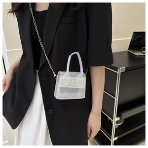 Petit sac carré transparent avec bandoulière en chaîne dorée porté par un mannequin