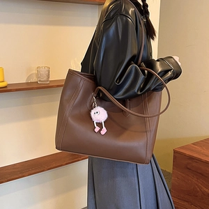 Minimalist dark brown leather tote bag with a pink plush monster charm on model