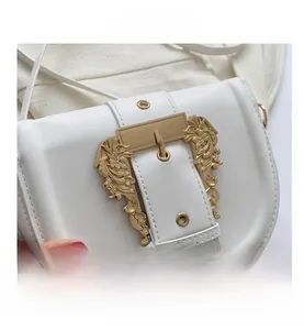 Close-up of vintage gold metal buckle with ornate floral engraving on white leather saddle bag