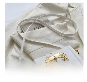 Close-up of white leather saddle bag featuring a large baroque gold embossed buckle