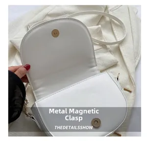 Detail showing the magnetic golden hardware closure on a white semi-circle saddle bag