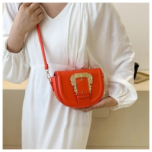 Detail of a bright orange saddle bag featuring a bold golden baroque style buckle