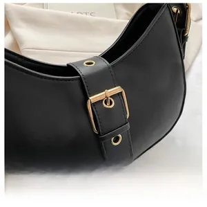 Detail of matte black crescent bag with large gold square buckle and eyelet strap