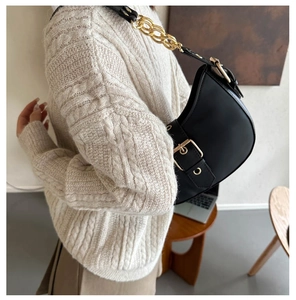 Close-up of black crescent moon bag with thick gold chain worn with a beige sweater