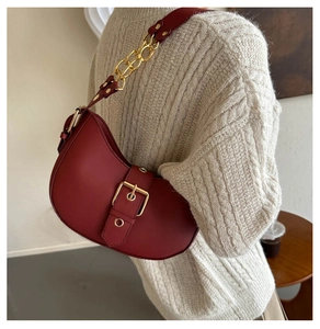 Close-up of vintage burgundy crescent shoulder bag with gold buckle on knit sweater