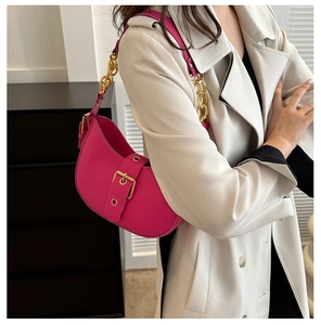Close-up of fuchsia crescent shoulder bag with glossy leather and gold buckle