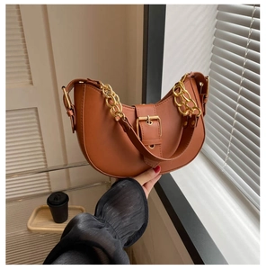Close-up of caramel hobo bag with gold metal chain and buckle in natural light