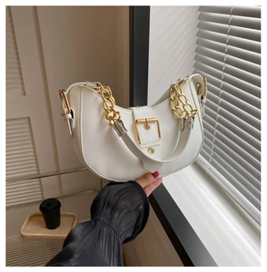 Detail of white half-moon underarm bag featuring a bold gold chain and buckle strap