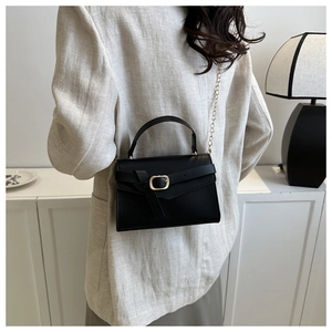 Détail d'un sac bandoulière noir mat avec chaîne dorée porté par un mannequin