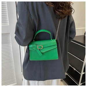 Close-up of vibrant green mini bag with gold buckle detail and chain strap on grey suit