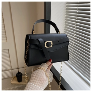 Détail d'un sac bandoulière noir avec chaîne dorée et poignée, porté par un mannequin