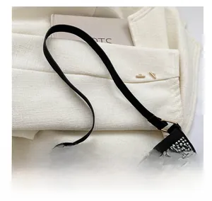 Dettaglio della borsa a tracolla con strass neri su sfondo blazer crema chic