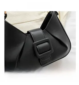 Detail view of the black retro shoulder bag featuring a large square buckle and side pleats
