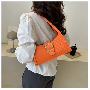Dettaglio di una borsa baguette in pelle trapuntata arancione con grande fibbia quadrata dorata