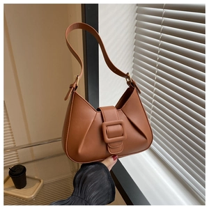 Detail of caramel brown faux leather underarm bag featuring a large square buckle and side pleats