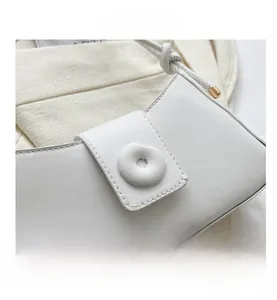 Detail of white minimalist underarm bag featuring a round padded buckle and gold accents