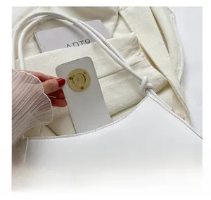 Close-up of golden magnetic buckle on cream crescent shoulder bag with smooth faux leather