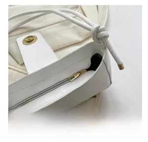 Detail of white leather shoulder bag featuring gold zipper, magnetic clasp and knot strap