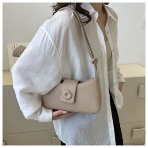 Minimalist beige leather shoulder bag with decorative round buckle on a model