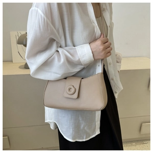 Detail of minimalist beige baguette shoulder bag featuring a circular clasp and matte finish