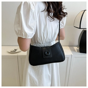 Close-up of minimalist black matte leather baguette bag worn by model in chic interior