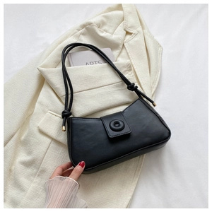 Détail du sac sous le bras en cuir noir mat avec boucle dorée sur un blazer beige
