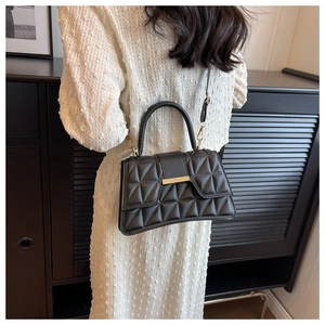 Detalle de bolso bandolera acolchado negro con herrajes dorados en vestido blanco