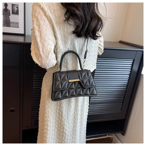 Elegante bolso acolchado negro con detalles dorados llevado al hombro en un interior