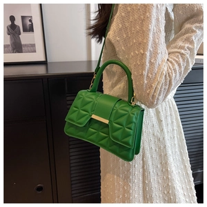 Bolso bandolera acolchado verde con hebilla dorada sobre un vestido blanco con textura