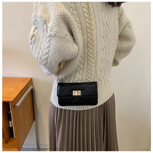 Detail of a black quilted chain bag with a gold twist lock on a beige knit sweater