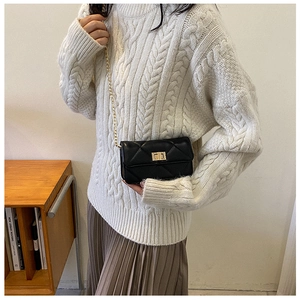 Detail of a black quilted chain bag featuring a gold square lock on a textured crossbody strap