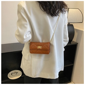 Detail of quilted brown chain crossbody bag with gold lock on white blazer model