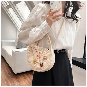 Détail d'un sac rond en paille avec broderies florales et nœud en ruban de dentelle