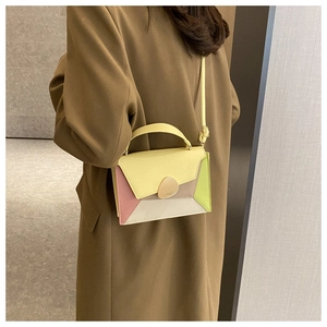 Detail of color-block square crossbody bag with pebble metal buckle on a brown trench coat