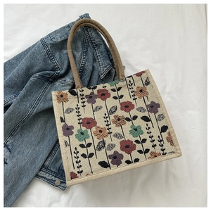 Detail of floral canvas tote bag featuring thick rope handles on a white fabric background