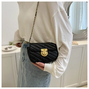 Detail of a black quilted crossbody bag with a gold T-shaped clasp and chain strap