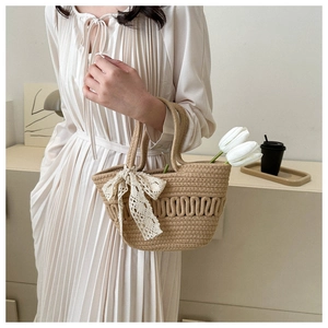 Detail of woven straw tote bag with wavy texture and cream lace bow charm detail